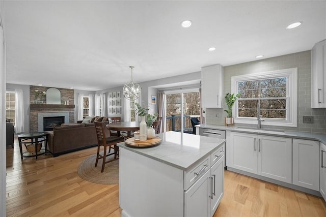 kitchen featuring light wood-type flooring, a sink, backsplash, recessed lighting, and a brick fireplace