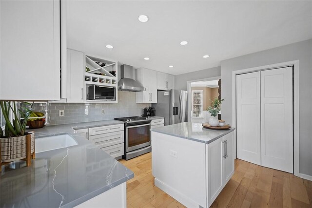 kitchen featuring white cabinetry, wall chimney range hood, light wood-style floors, and appliances with stainless steel finishes