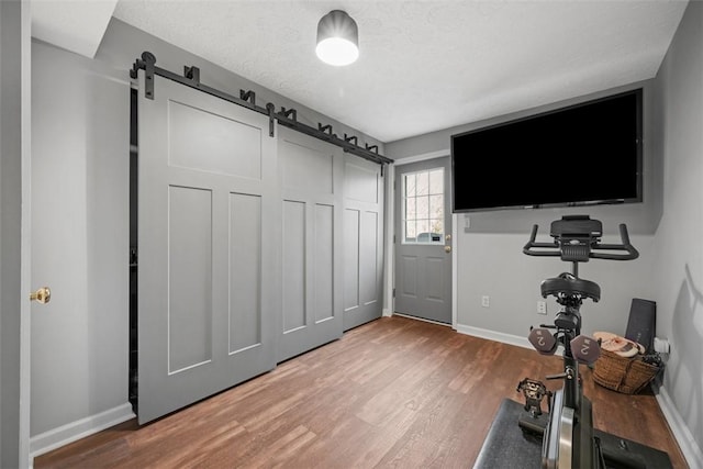 workout room with a textured ceiling, baseboards, a barn door, and wood finished floors