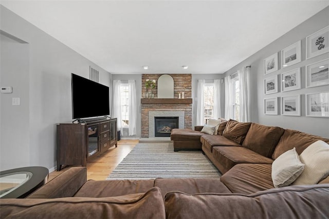 living room featuring a wealth of natural light, a stone fireplace, and light wood-style flooring