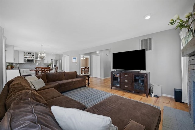 living room featuring light wood-style flooring, a fireplace with flush hearth, baseboards, and visible vents