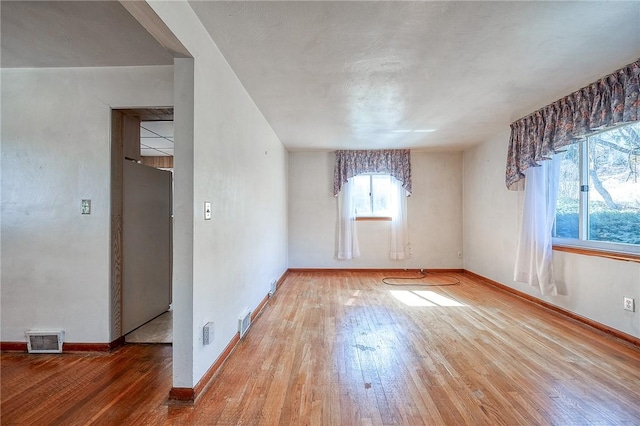 empty room with visible vents, baseboards, and hardwood / wood-style flooring