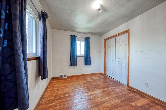 unfurnished bedroom featuring visible vents, baseboards, a closet, and wood finished floors