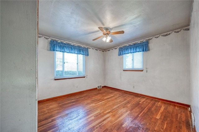 empty room with a wealth of natural light, baseboards, wood finished floors, and a ceiling fan