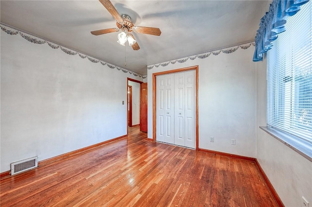 unfurnished bedroom with visible vents, wood finished floors, a closet, baseboards, and ceiling fan