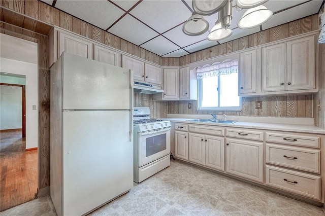 kitchen with white appliances, a sink, light countertops, under cabinet range hood, and a chandelier