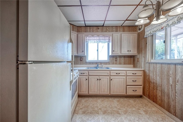 kitchen with a sink, a drop ceiling, white appliances, wooden walls, and light countertops