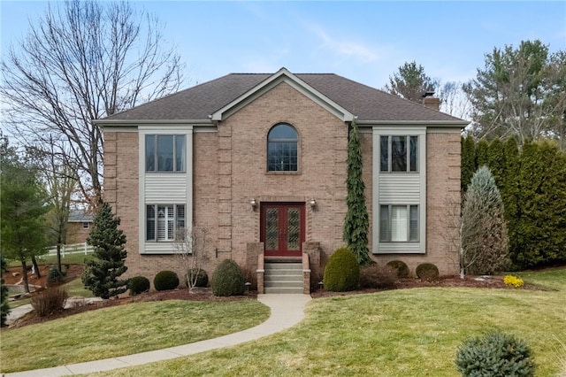 view of front of house with a front yard, roof with shingles, a chimney, french doors, and brick siding