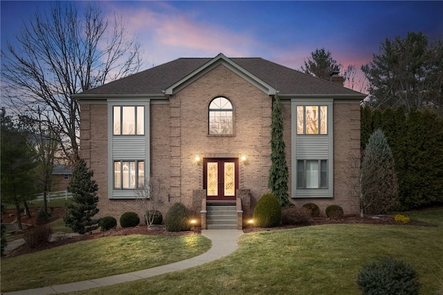 colonial home with a shingled roof, a chimney, a front lawn, french doors, and brick siding