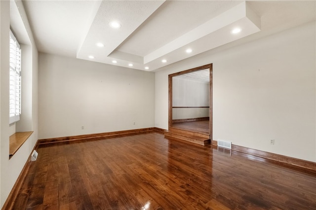 empty room featuring visible vents, baseboards, recessed lighting, wood finished floors, and a raised ceiling