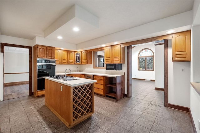 kitchen featuring baseboards, recessed lighting, a kitchen island with sink, black appliances, and light countertops