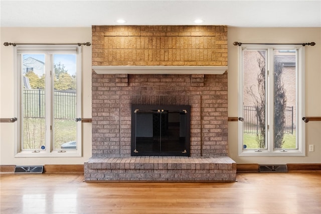 unfurnished living room featuring visible vents, baseboards, a brick fireplace, and wood finished floors