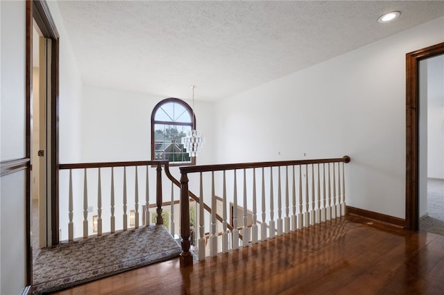 corridor with wood finished floors, baseboards, a textured ceiling, an upstairs landing, and a chandelier