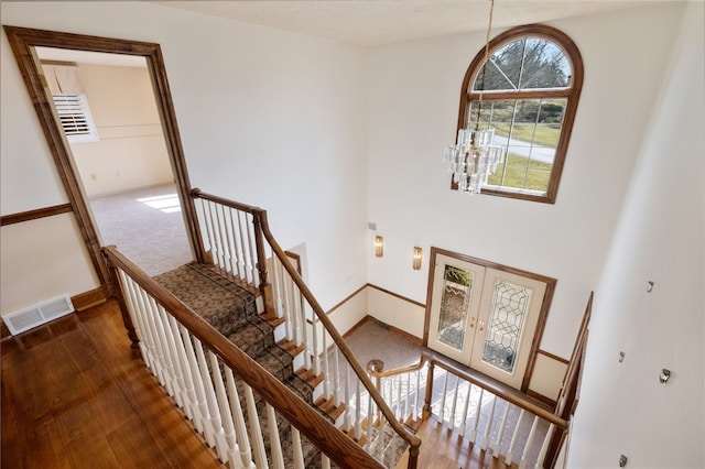 staircase with wood finished floors, french doors, visible vents, and baseboards