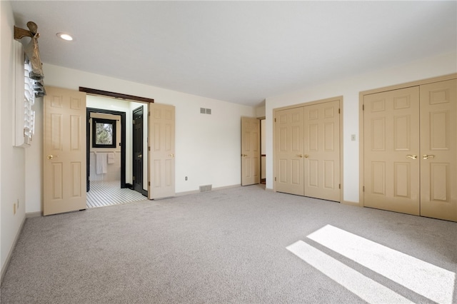 unfurnished bedroom with visible vents, light colored carpet, multiple closets, and baseboards