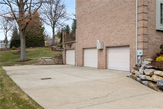 view of side of home with a garage, brick siding, a yard, and driveway