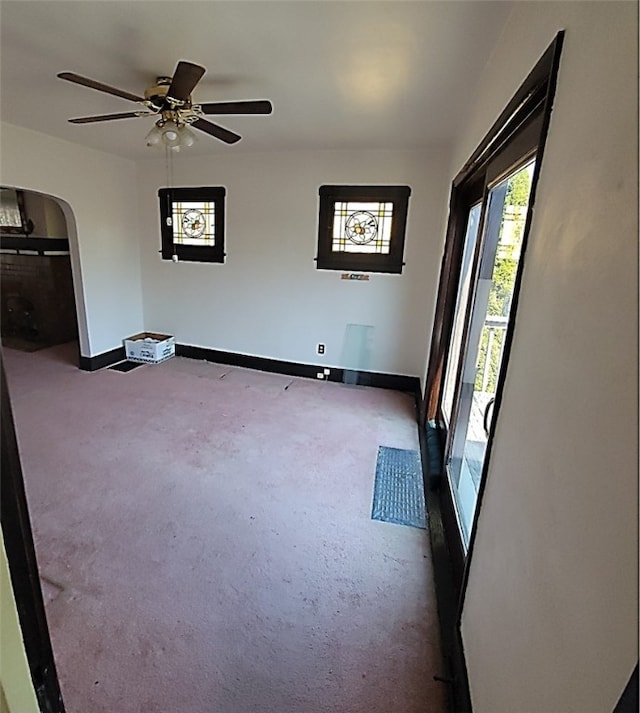 unfurnished room featuring baseboards, arched walkways, and ceiling fan