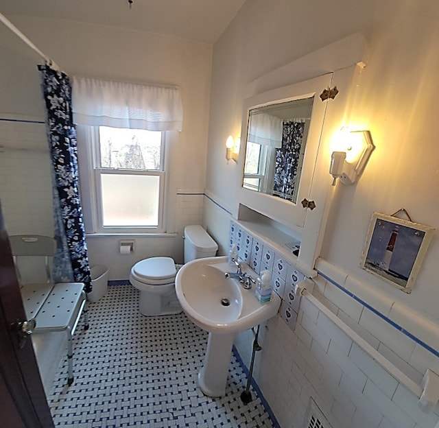 full bathroom with a wainscoted wall, curtained shower, toilet, and tile walls