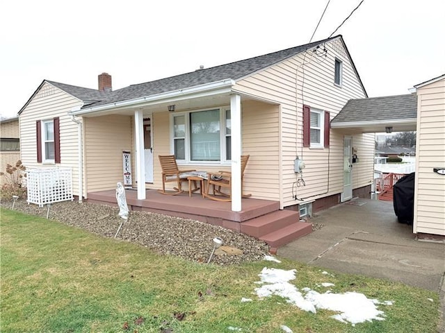 view of front of property with an attached carport, a shingled roof, a front lawn, a porch, and concrete driveway