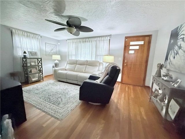 living area with ceiling fan, a textured ceiling, and wood finished floors