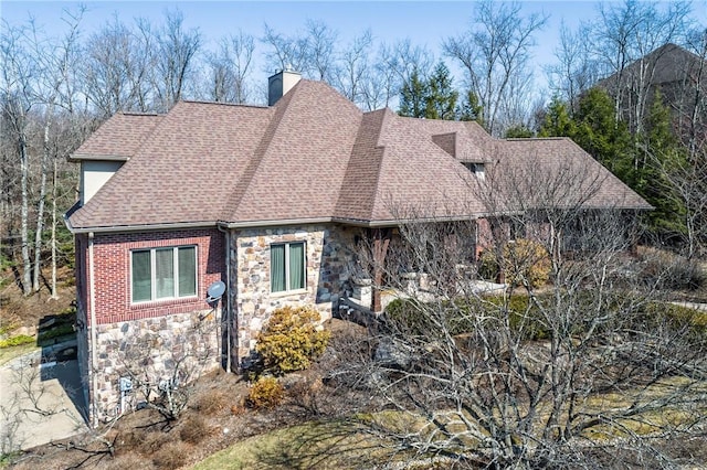 view of front of property featuring brick siding, stone siding, a chimney, and a shingled roof