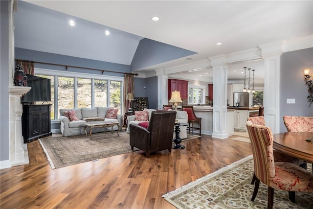 living area with crown molding, vaulted ceiling, decorative columns, recessed lighting, and wood finished floors