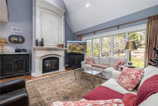 living room with visible vents, high vaulted ceiling, wood finished floors, and a glass covered fireplace