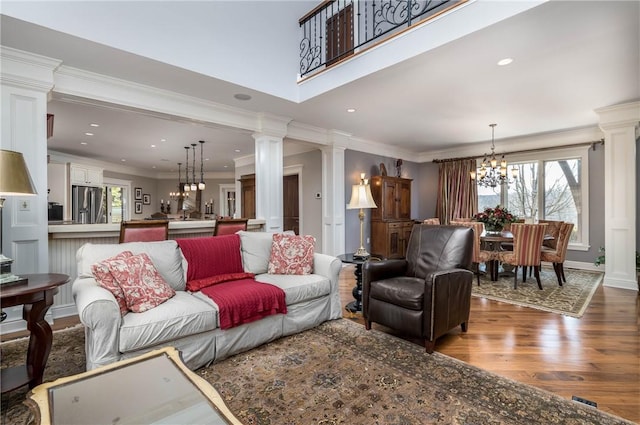 living room with ornamental molding, wood finished floors, an inviting chandelier, and decorative columns