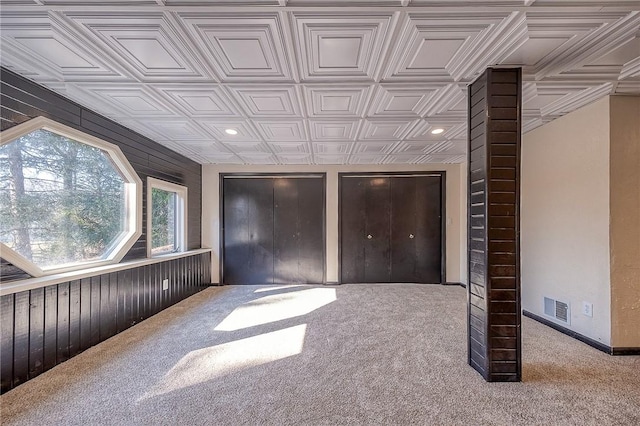 unfurnished bedroom featuring visible vents, an ornate ceiling, wooden walls, and carpet floors