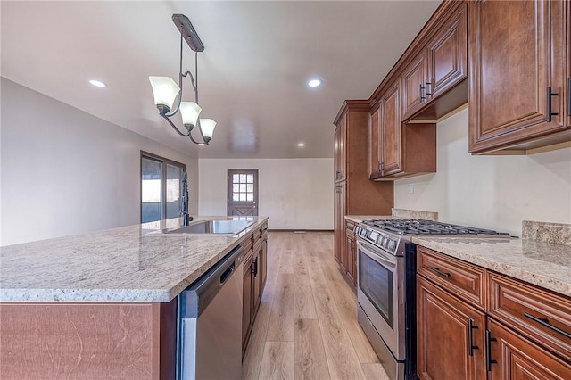 kitchen featuring pendant lighting, light wood-style flooring, an island with sink, a sink, and appliances with stainless steel finishes