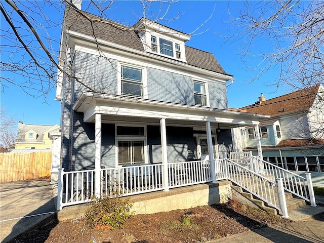 view of front of house featuring a porch, fence, brick siding, and roof with shingles