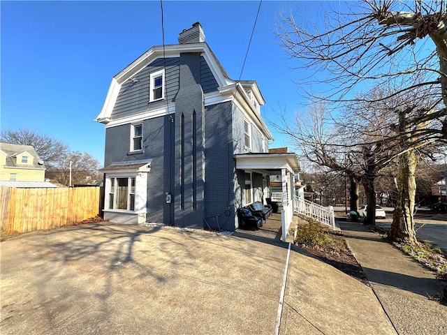 exterior space with a gambrel roof, brick siding, a chimney, and fence