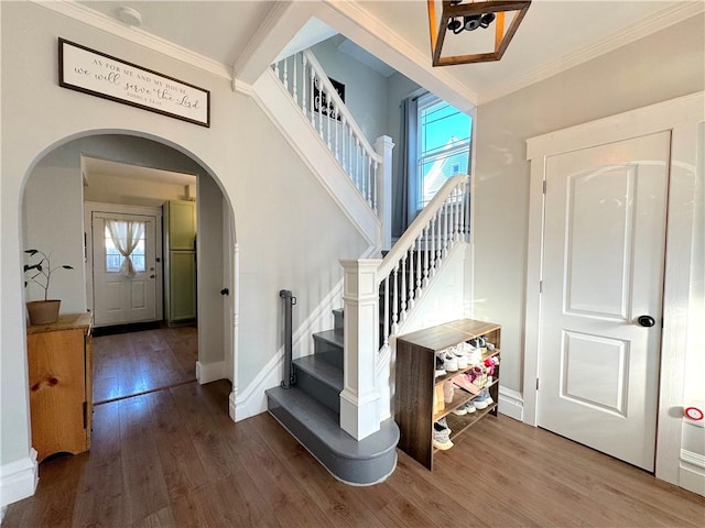 entrance foyer featuring ornamental molding, wood finished floors, arched walkways, baseboards, and stairs