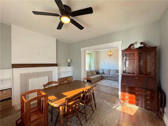 dining space with a ceiling fan, wood finished floors, and a fireplace