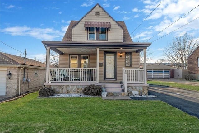 view of front of home featuring a porch, a shingled roof, a front lawn, an outdoor structure, and aphalt driveway