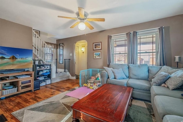 living area featuring stairway, arched walkways, wood finished floors, and a ceiling fan