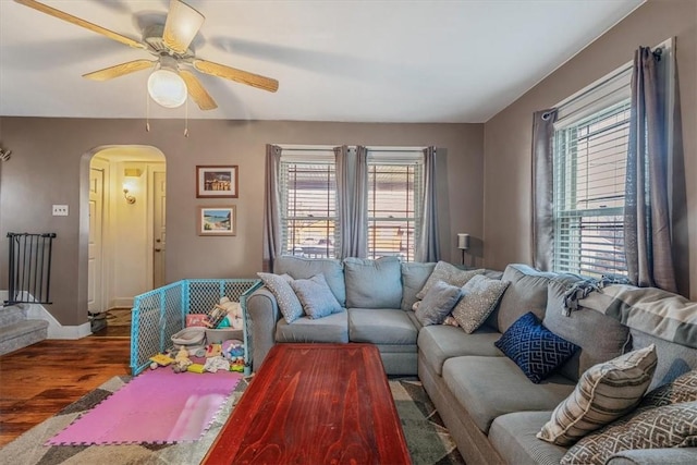 living room featuring baseboards, wood finished floors, arched walkways, and ceiling fan