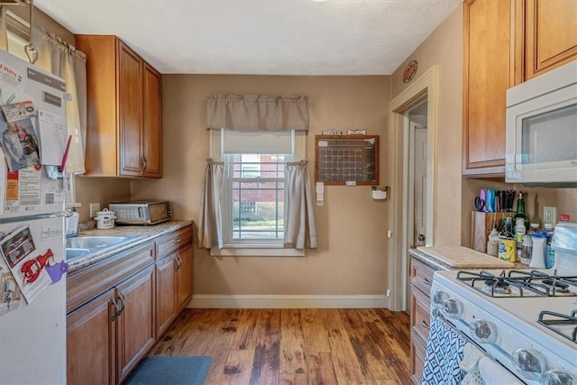 kitchen featuring baseboards, light countertops, brown cabinets, light wood-style floors, and white appliances