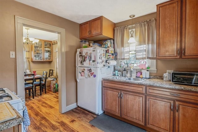 kitchen with light wood-type flooring, brown cabinets, a sink, white appliances, and a toaster