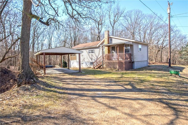 view of front of home with a front lawn, driveway, covered porch, a detached carport, and a chimney