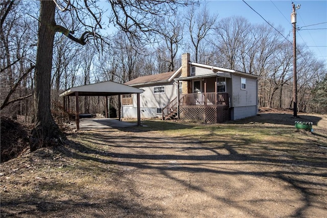 exterior space featuring a detached carport, covered porch, a chimney, and dirt driveway