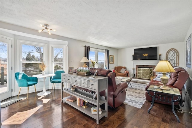 living area with a brick fireplace, wood finished floors, baseboards, and a textured ceiling