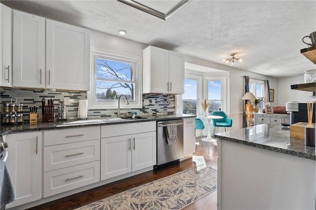 kitchen featuring a wealth of natural light, a sink, dark stone countertops, white cabinetry, and dishwasher