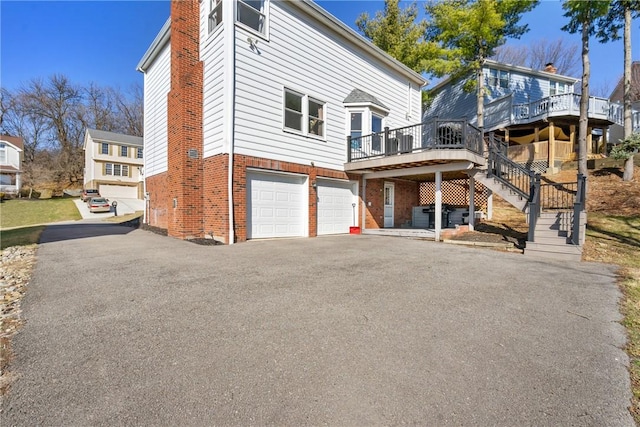 exterior space with aphalt driveway, stairs, an attached garage, brick siding, and a chimney