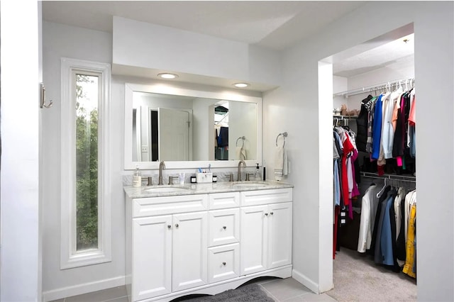 bathroom with double vanity, a spacious closet, baseboards, and a sink