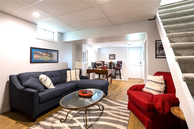 living area with baseboards, a paneled ceiling, wood finished floors, and stairs