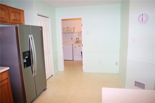 kitchen featuring visible vents, washer and clothes dryer, light floors, stainless steel refrigerator with ice dispenser, and brown cabinetry