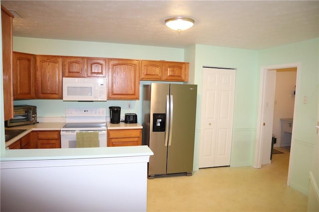 kitchen with white appliances, brown cabinetry, a peninsula, a toaster, and light countertops