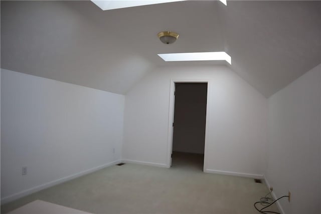 additional living space with visible vents, vaulted ceiling with skylight, light colored carpet, and baseboards