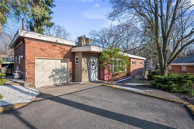 view of front of home with brick siding, an attached garage, a chimney, and aphalt driveway